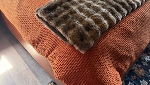 Ein Bett mit orangefarbener Bettwäsche, einer grauen Decke und einem gemusterten Kopfkissen.