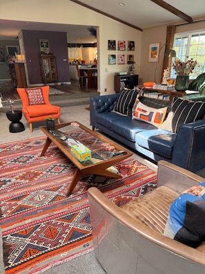 Una sala de estar con sofá azul, sillón naranja, alfombra estampada y una mesita de centro con una caja y un control remoto.