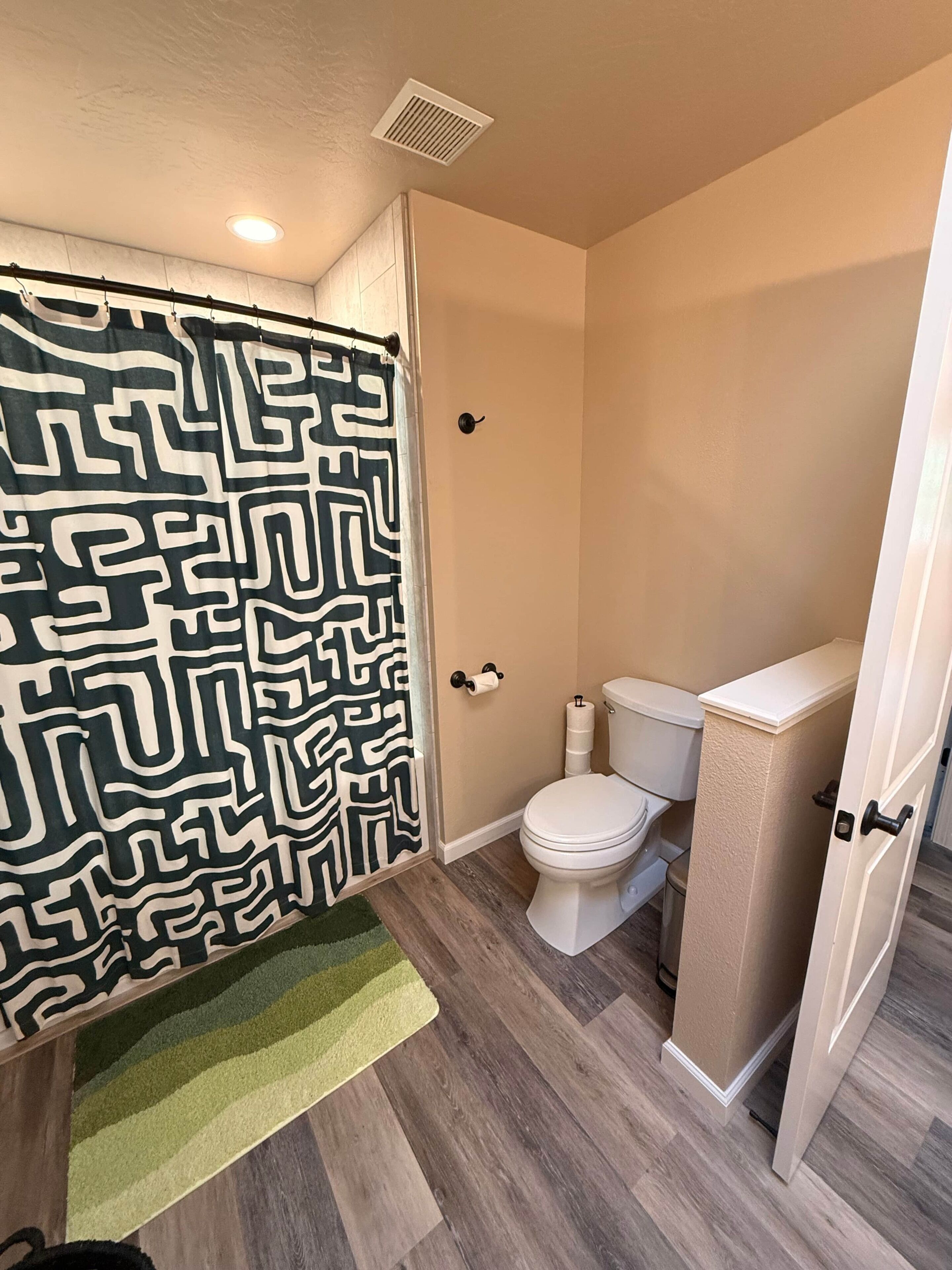 A bathroom with a patterned shower curtain, a toilet, and a wooden floor.