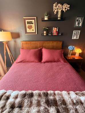 A bed with a red blanket, a wooden headboard, and a fluffy throw at the foot of the bed. - Hudson Queen Room at Mountain Daddies B&B (Oakhurst)