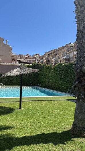 Una piscina amb una ombra de palla, envoltada per gespa cuidada i una tanca.