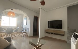 Un saló modern amb una taula de centre de vidre, un televisor pantalla plana muntat a la paret i una zona de seients amb cadires i un sofà.