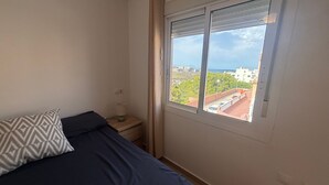 A bedroom with a bed, a bedside table, a lamp, and a window with a city view.