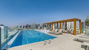 En pool på taket med solstolar och en pergola, med utsikt över stadens skyline.