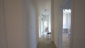 A hallway with a light wooden floor, white walls, and a door leading to a room with a bed and a chair. - 118 m2 apartment, ideal for up to 7 people, on the 2nd floor of a building with lift.Located in San Giuliano Mare, north of the canal port and a few minutes from the historic center, it enjoys a strategic position that allows you to easily reach the beac (Rimini)
