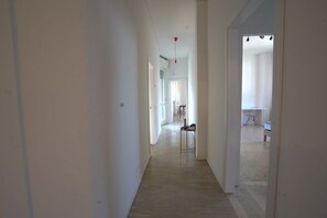 A hallway with a light wooden floor, white walls, and a door leading to a room with a bed and a chair. - 118 m2 apartment, ideal for up to 7 people, on the 2nd floor of a building with lift.Located in San Giuliano Mare, north of the canal port and a few minutes from the historic center, it enjoys a strategic position that allows you to easily reach the beac (Rimini)