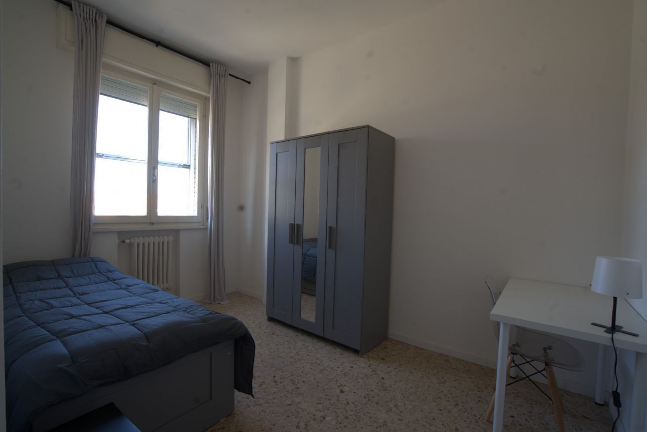 A bedroom with a bed, a wardrobe, a desk, and a radiator.