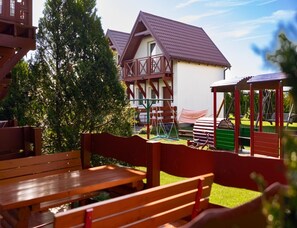Eine Holzbank und eine Schaukel in einem Park, im Hintergrund ein Gebäude.