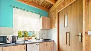 Cocina compacta con armarios de madera, lavavajillas, microondas, pileta y ventana con cortina.