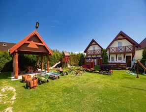 Ein Spielplatz mit unterschiedlicher Spielausstattung, einem überdachten Sitzbereich und einer Rasenfläche.