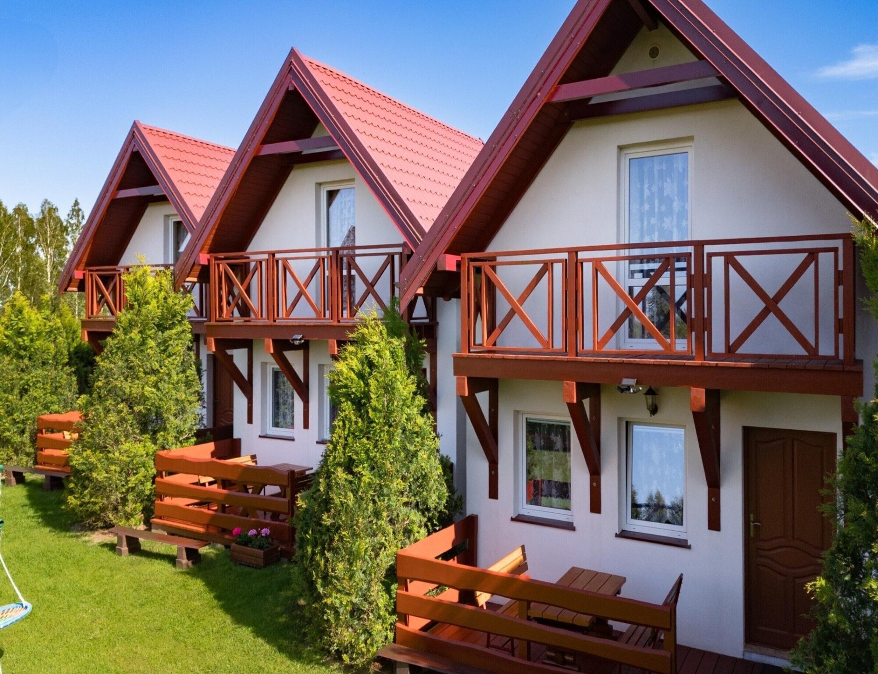 A row of chalet-style cabins with wooden balconies, a grassy lawn, and a clear sky.