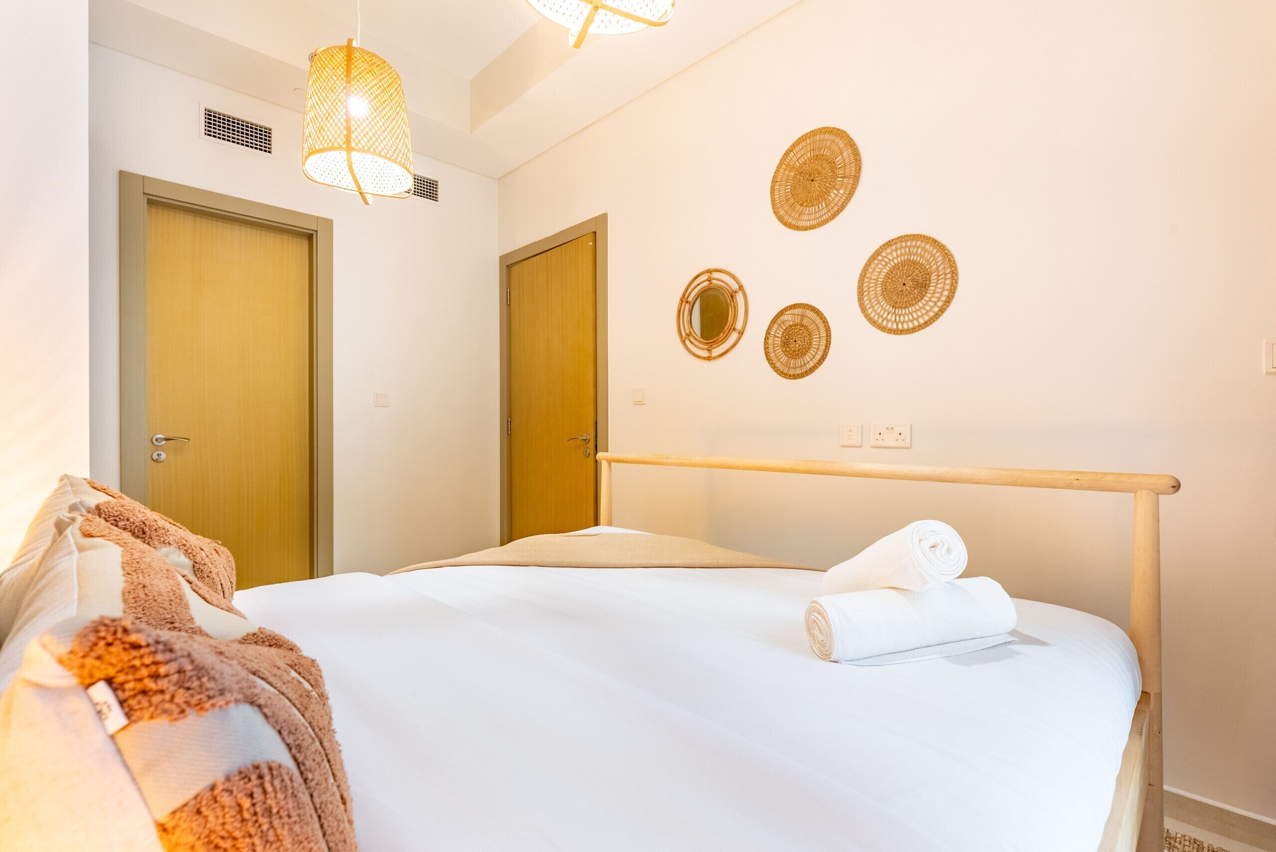 Ein Hotelzimmer mit einem Bett, zwei Türen, einem an der Wand befestigten Spiegel und drei gewebten Wandbildern.