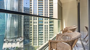 Uma varanda com cadeiras de vime, guarda-corpo de vidro e vista para edifícios altos.