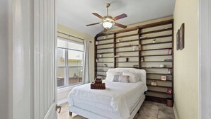 Een slaapkamer met een bed, een plafondventilator, een raam en een boekenkast.