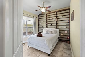 A bedroom with a bed, a ceiling fan, a window, and a bookshelf.