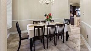 Een eetkamer met een kroonluchter, een ronde tafel en zes stoelen.