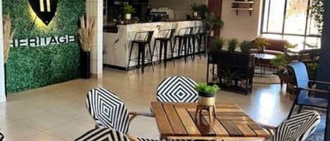A modern hotel lobby with a green wall, a bar area, and a dining space with patterned chairs.