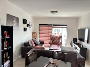 A living room with a sofa, armchair, dining table, bookshelf, and a television. - Fourways Retreat Your Home Away From Home (Johannesburg)