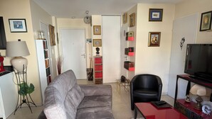 A living room with a grey sofa, a red table, a black chair, a TV, and a bookshelf with red and black books. - Beautiful apartment with a piano (Sainte-Maxime)
