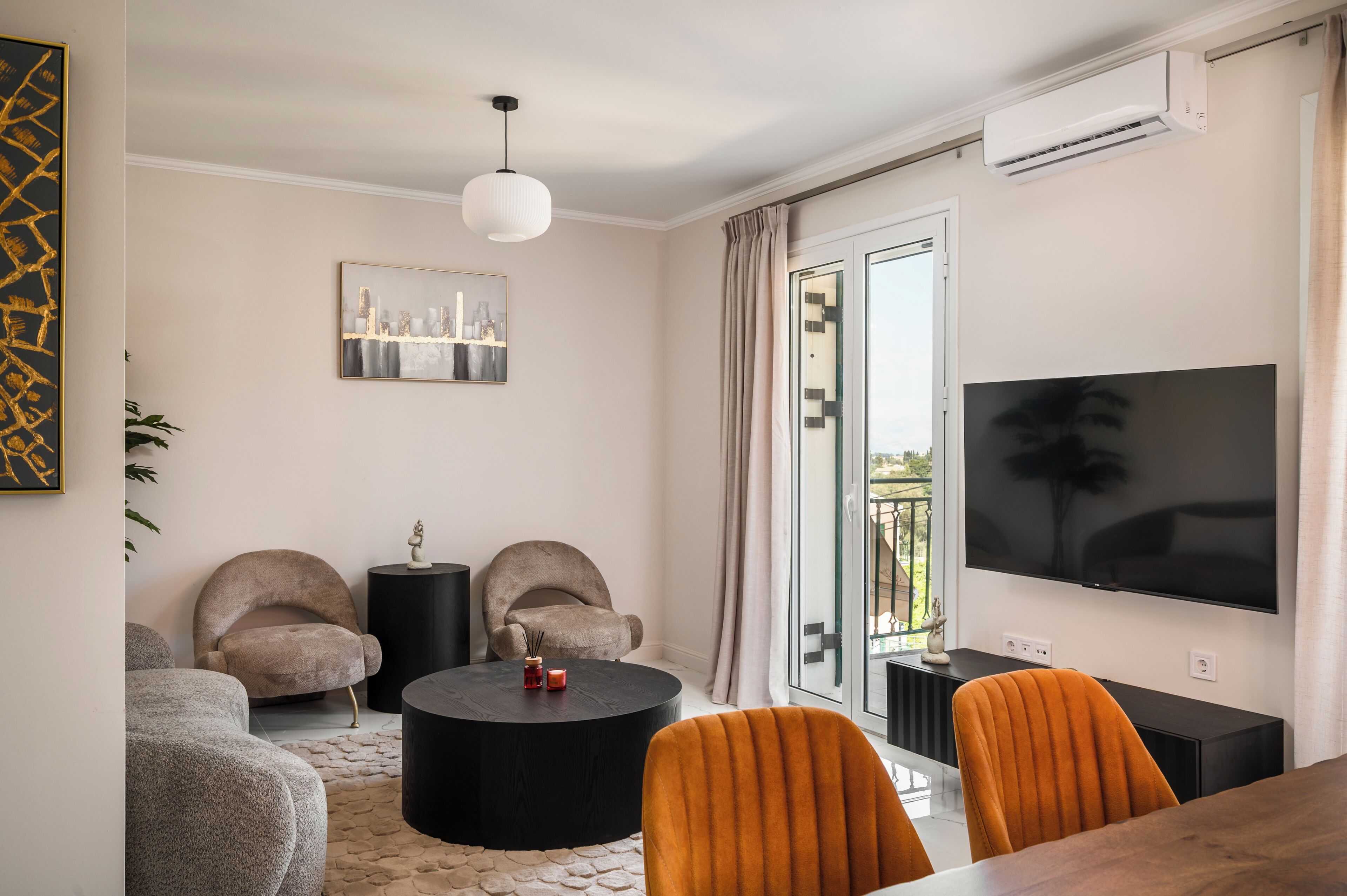 Una sala de estar moderna con un televisor de pantalla plana, dos sillones, una mesa de centro redonda y una mesa de comedor.