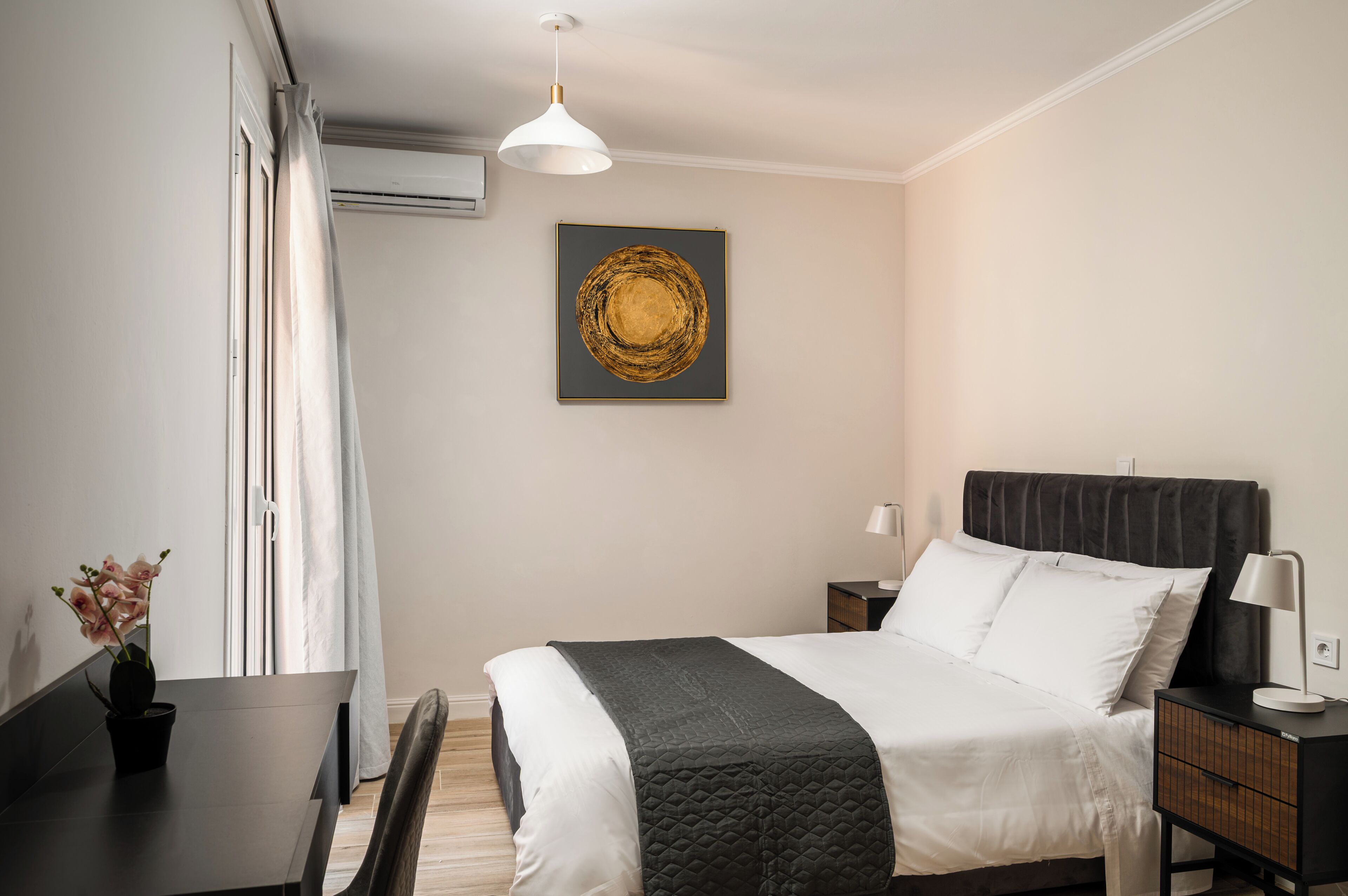 A hotel room with a bed, bedside table, lamp, and a wall-mounted artwork.