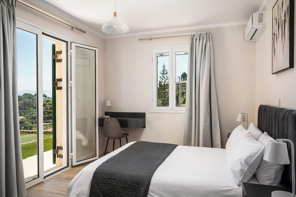 A bedroom with a bed, a desk, a chair, a window, and an air conditioning unit.