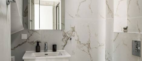 Un baño con pared de mármol, un lavamanos blanco, un espejo y un inodoro.