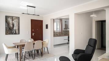 Una sala de estar moderna con comedor, un sillón negro y una cocina al fondo.