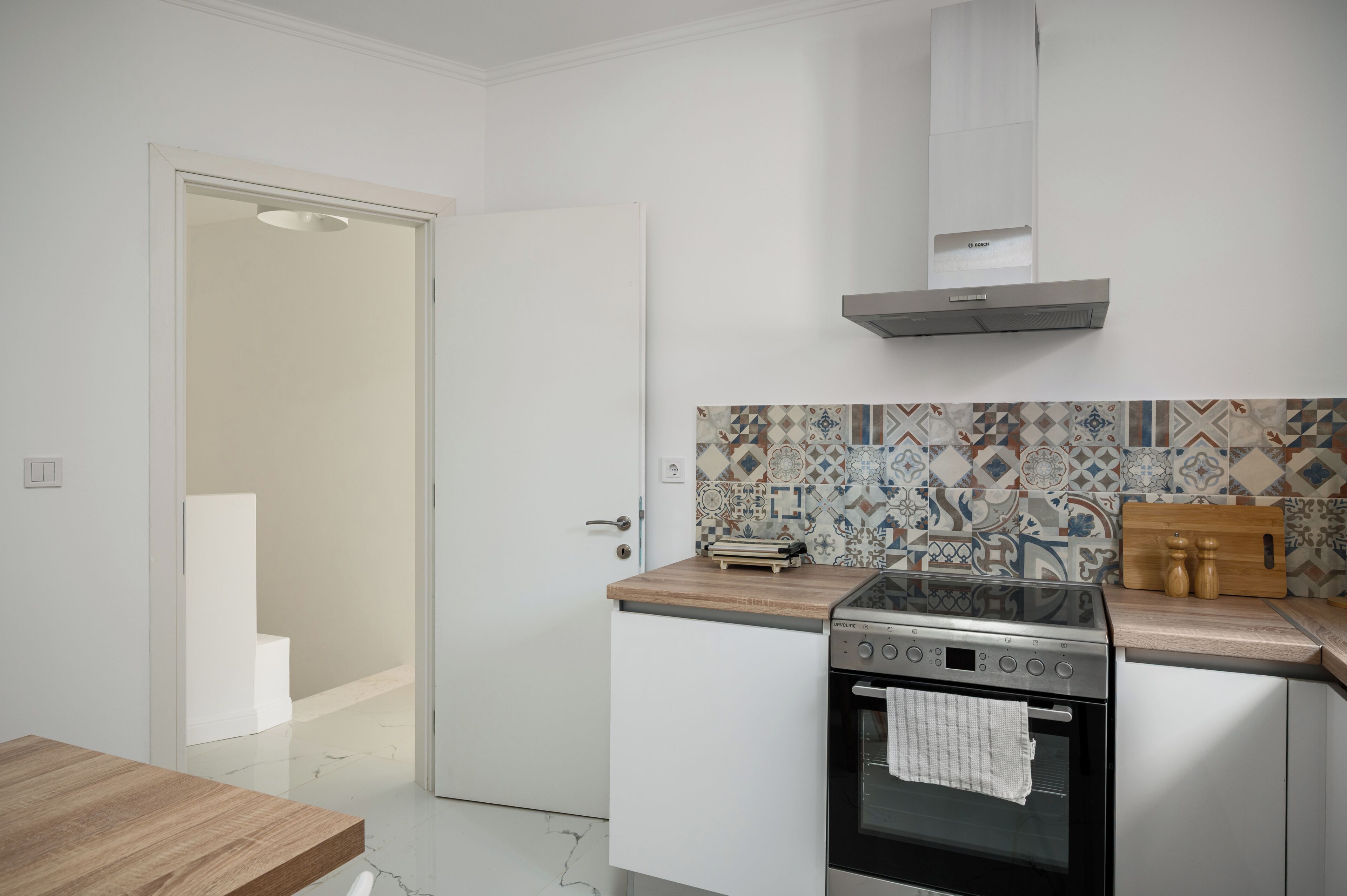 A modern kitchen with white cabinetry, a stainless steel stove, and a patterned backsplash.
