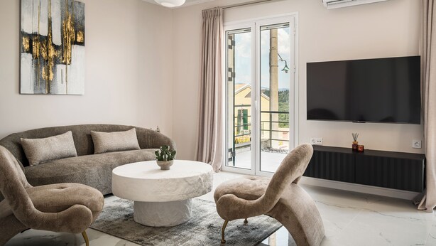 A modern living room with a sofa, two armchairs, a coffee table, a flat-screen TV, and a large window.