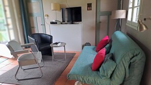 Un salon avec un canapé, des fauteuils, un téléviseur et une lampe.