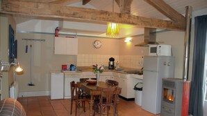 Une cuisine chaleureuse avec des poutres en bois, une table à manger, des chaises, un poêle et une horloge au mur.