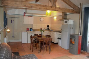 Une cuisine chaleureuse avec des poutres en bois, une table à manger, des chaises, un poêle et une horloge au mur.