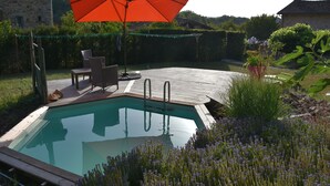 Une piscine avec une terrasse en bois, une chaise et un parasol.