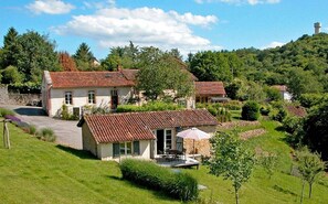 Une maison de campagne avec un toit en tuiles, une allée pavée et une petite terrasse aménagée avec du mobilier d’extérieur.
