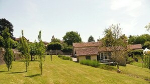 Un quartier résidentiel avec une pelouse verdoyante, un petit bâtiment doté d’un toit en tuiles et, au loin, une église surmontée d’un clocher.