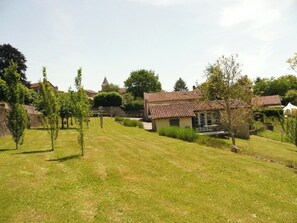 Un quartier résidentiel avec une pelouse verdoyante, un petit bâtiment doté d’un toit en tuiles et, au loin, une église surmontée d’un clocher.