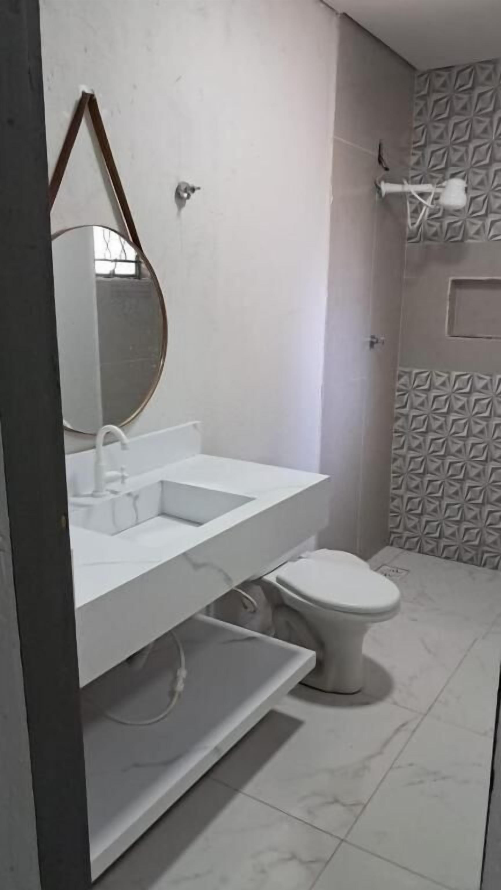 Casa de banho com lavatório branco, espelho e sanita.
