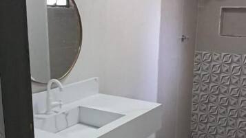 Casa de banho com lavatório branco, espelho e sanita.