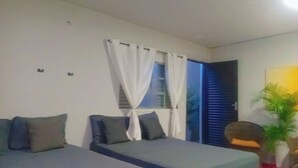 A bedroom with two beds, white curtains, a window, a door, and a potted plant. - Garden Monte Líbano (Rondonópolis)