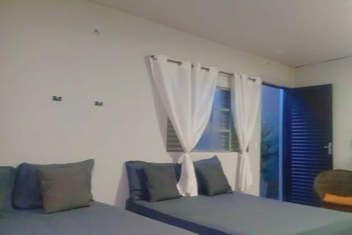 Un dormitorio con dos camas, cortinas blancas, una ventana, una puerta y una planta en maceta.