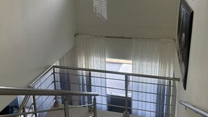 A staircase with metal railings, a hanging chandelier, a window with curtains, and a framed picture on the wall. - Belair Pool Villa w/ Rooftop & Island Views Oasis (Little Bay)