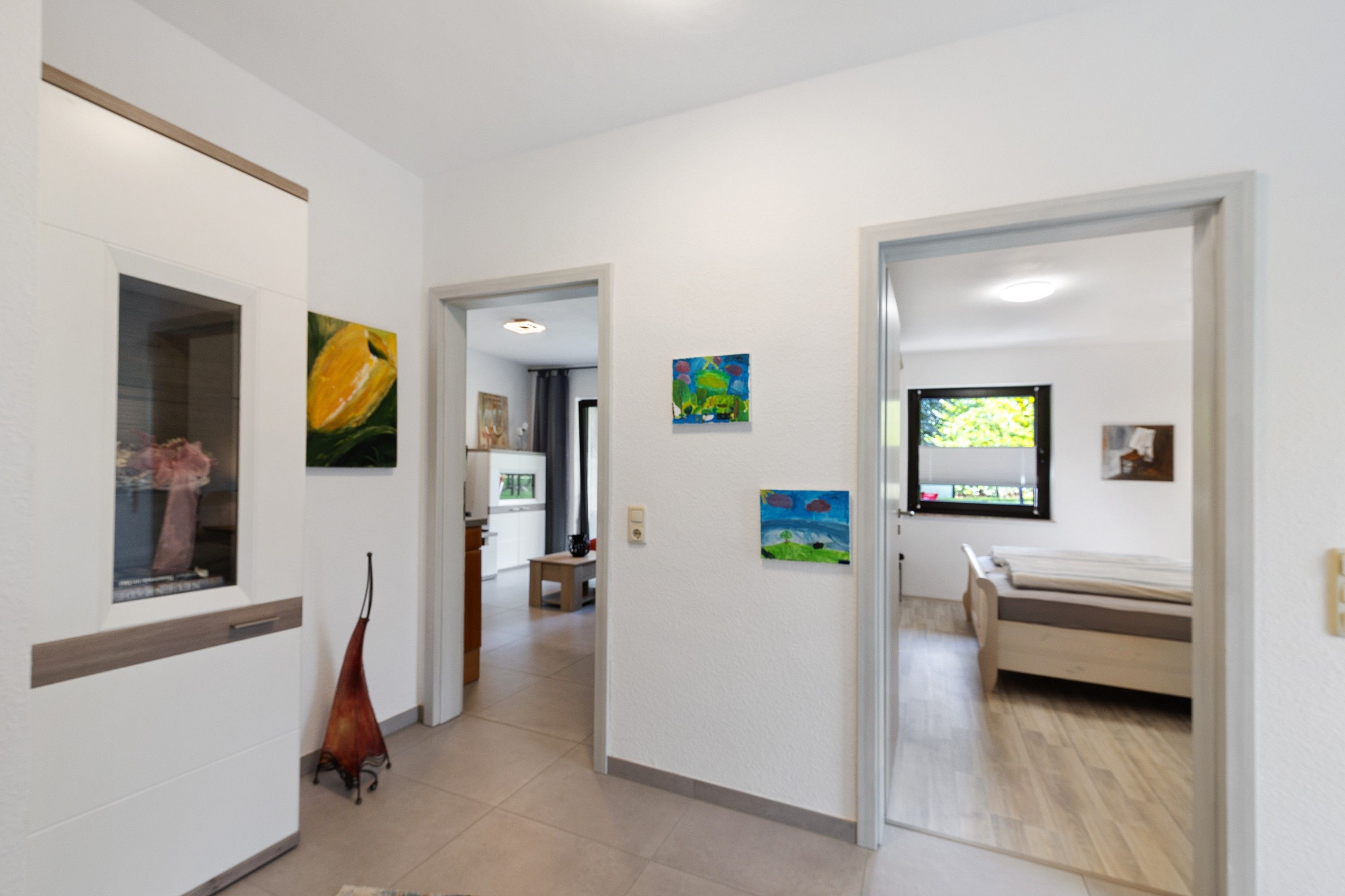 A hallway with a bed, a window, and artwork on the walls.