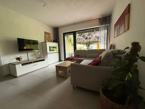 Ein modernes Wohnzimmer mit Fernseher, Sofa und großem Fenster.