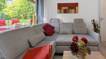 A modern living room with a grey sofa, red cushions, and a vase of flowers on a wooden table.