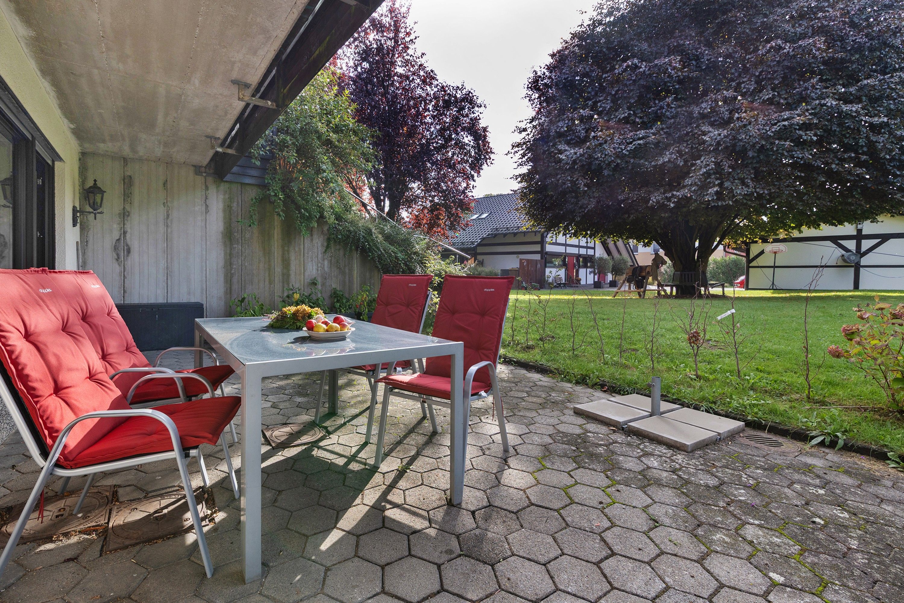 Ein Sitzbereich im Freien mit Tisch und Stühlen, ein kleiner Garten und ein Gebäude im Hintergrund.