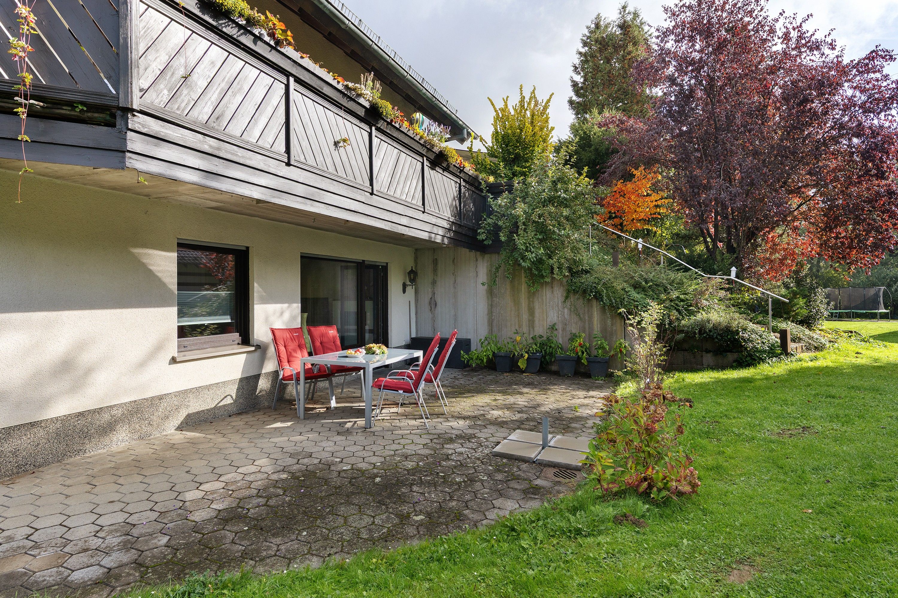 A house with a covered patio, a dining table with chairs, and a garden with various plants.