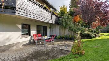 A house with a covered patio, a dining table with chairs, and a garden with various plants.
