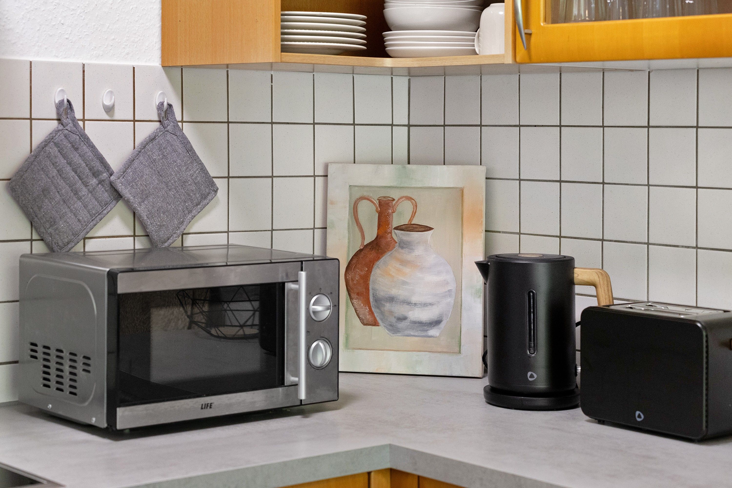 A kitchen with a microwave, toaster, and a painting on the wall.