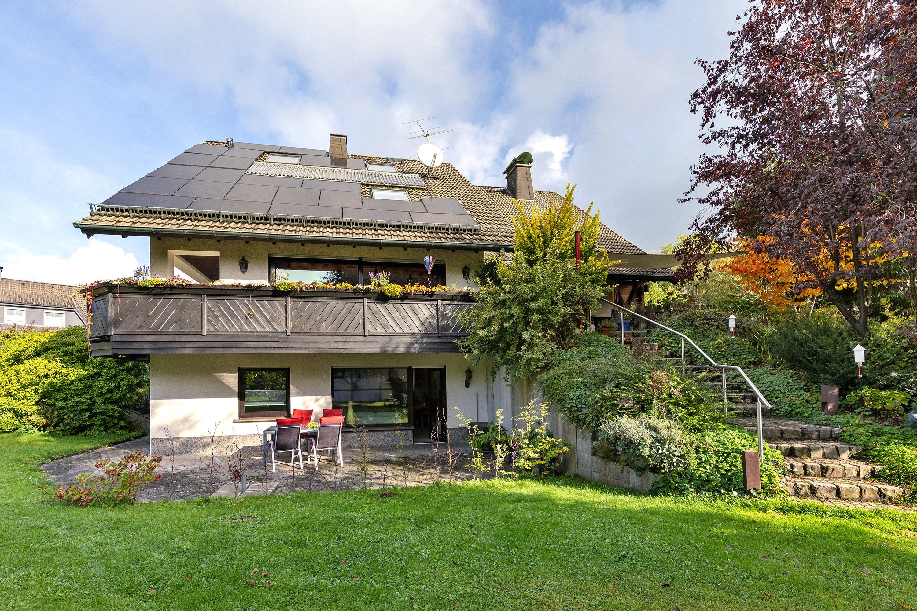 Une maison à deux étages avec un balcon, un jardin et un escalier menant à l’étage supérieur.